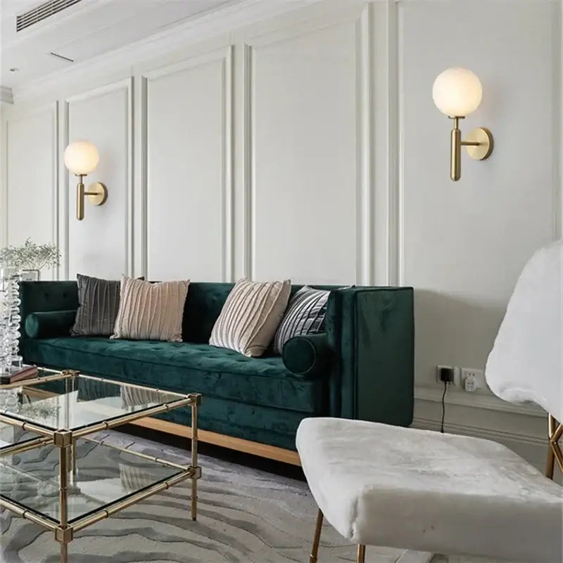 Deep emerald green velvet sofa with rolled arms and tufted backrest shown alongside decorbites glass ball wall lamp with brass and opaque globe