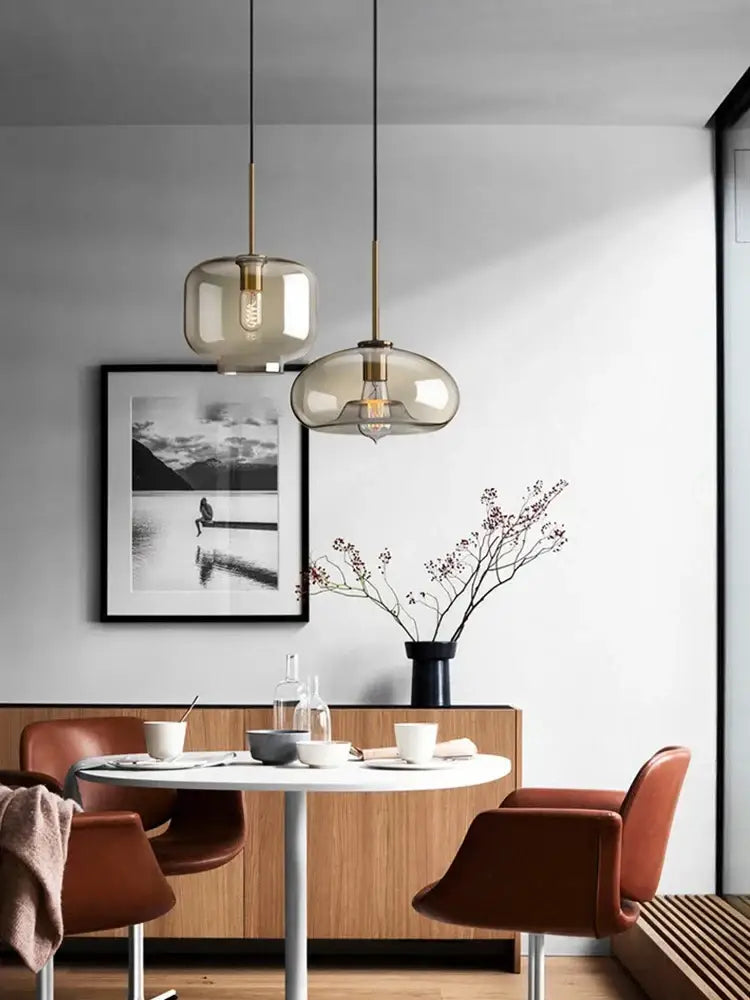 Two modern decorbites glass chandelier pendant lights with smoked glass and brass accents hang above a white table