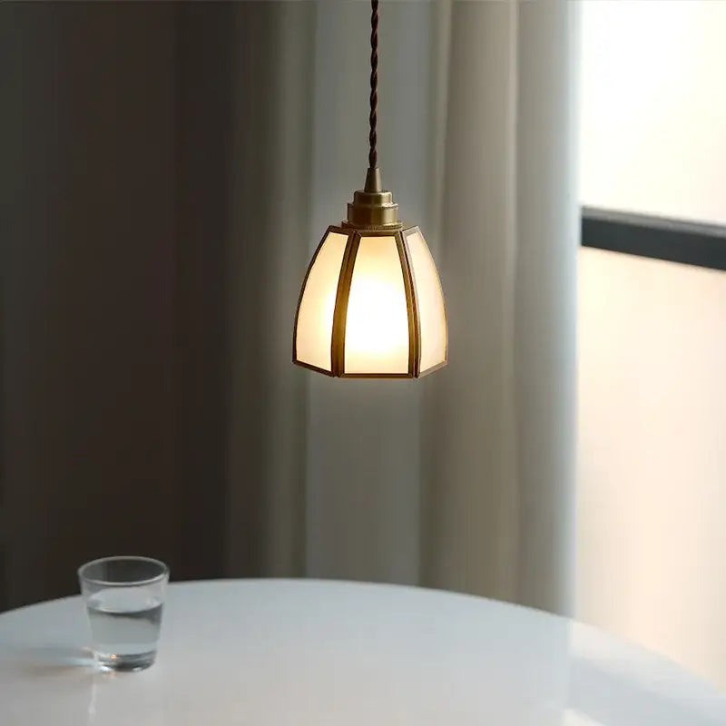 A warm-toned brass glass copper led pendant light with a hexagonal shade hangs from a twisted cord for dining rooms
