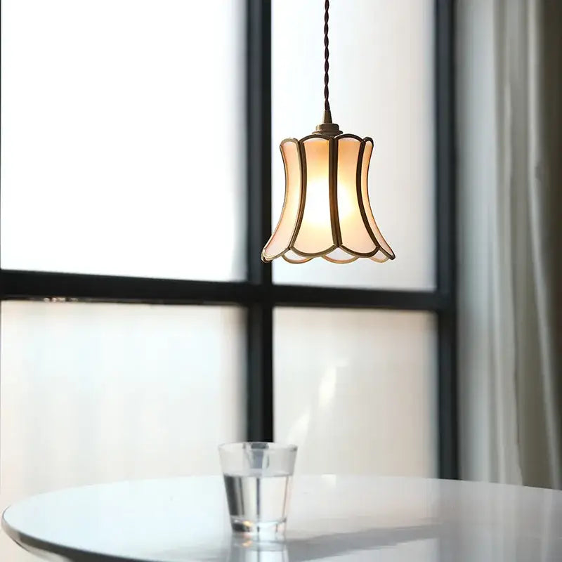 A warm-toned modern brass glass copper led pendant light with bell shape hanging from twisted cord for dining room