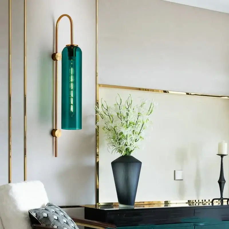 Modern brass glass sconce wall lamp featuring a teal glass cylinder in an arched brass frame for living room use