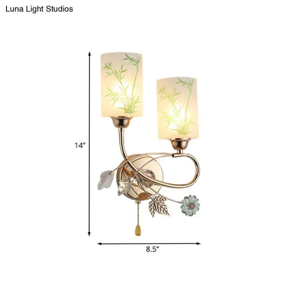 Modern brass wall lamp with glass shade, green bamboo leaf design, decorative metal accents, and pull chain for bedroom
