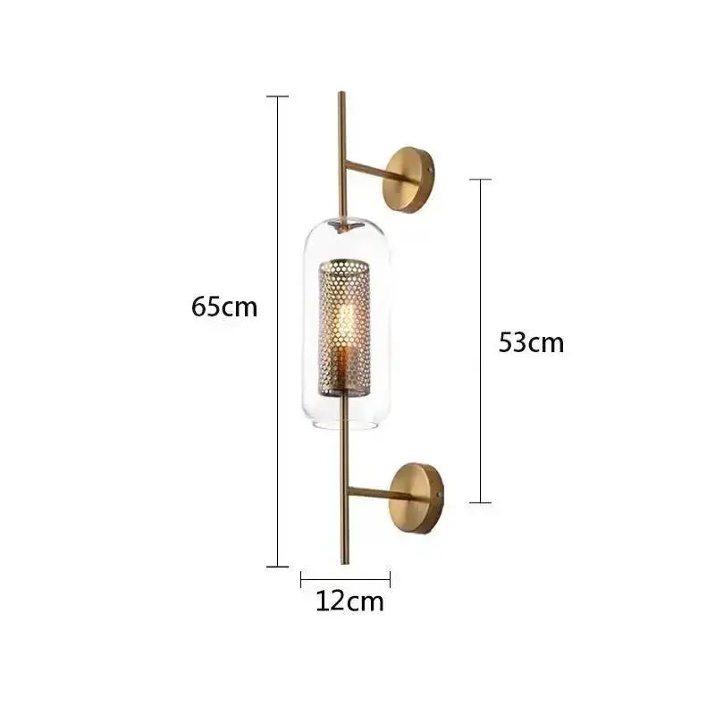 Modern brass glass wall lamp with a brass-finished sconce, clear glass cylinder, and perforated gold mesh shade for bedroom decorbites