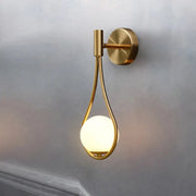 Modern brass glass wall lamp with a gold-toned teardrop frame and glowing bulb for bedroom lighting decorbites brass glass
