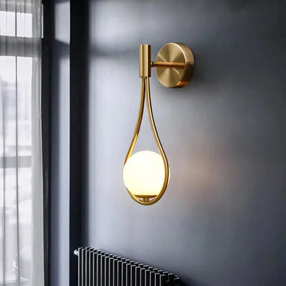Modern brass glass wall lamp with gold-toned teardrop frame and glowing spherical bulb for bedroom lighting decorbites brass glass