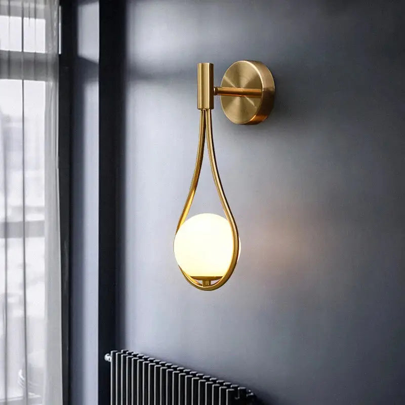Modern brass glass wall lamp with gold-toned teardrop frame and glowing spherical bulb for bedroom lighting decorbites brass glass