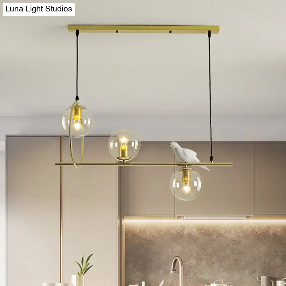 Modern brass global island lamp with gold-toned pendant, three glass globe bulbs, and white ceramic bird detail
