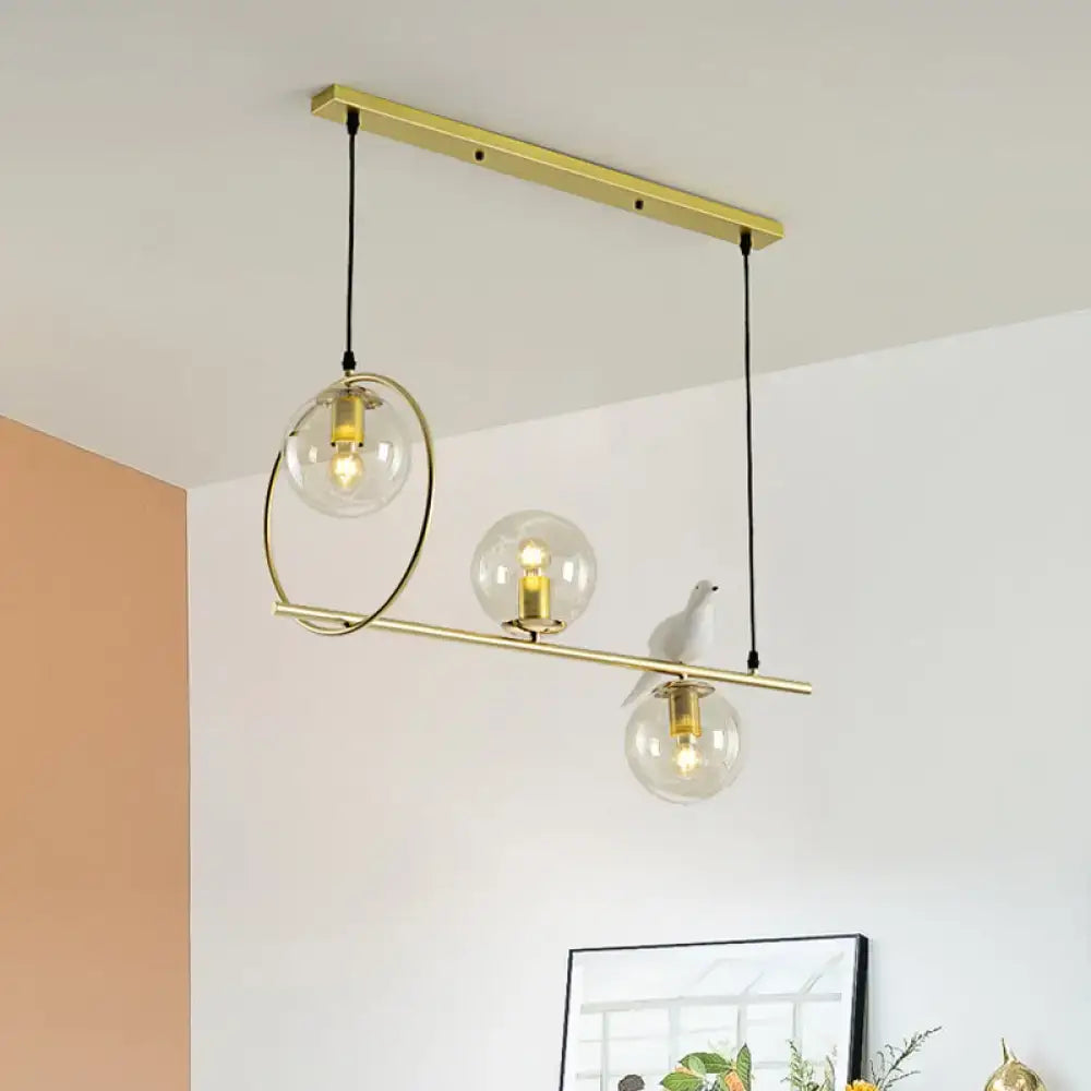 Modern brass global island lamp with three clear glass globes and a decorative white bird for dining room lighting