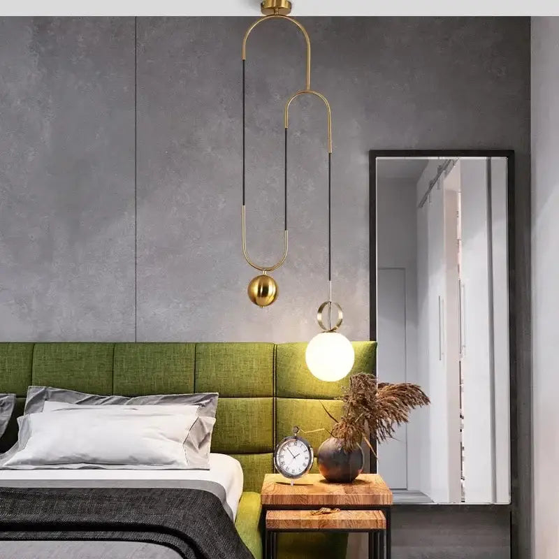 Modern brass golden glass ball pendant lamps with curved metal arms and spherical shades above green bed decorbites golden glass