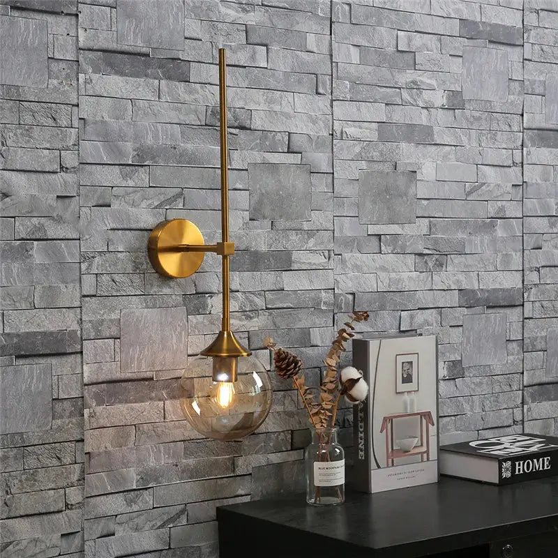 Modern brass golden glass ball wall lamp with slender gold-toned arm and spherical bulb for bedroom decorbites golden glass decor