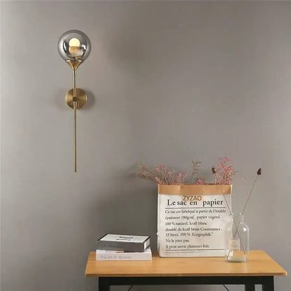 A sleek modern wall lamp with brushed brass finish and golden glass ball globe for bedroom decorbites golden glass