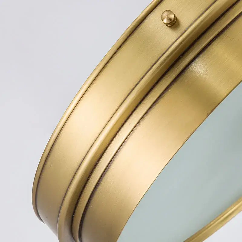 Brass led ceiling light with frosted glass and a brass-finished circular wall mirror featuring brushed metal frame ridges