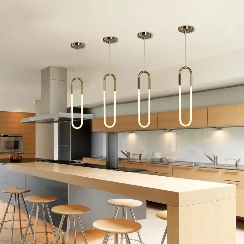 Four modern pendant lights with curved brass frames and glowing white led tubes in a modern brass led u-shaped bar chandelier