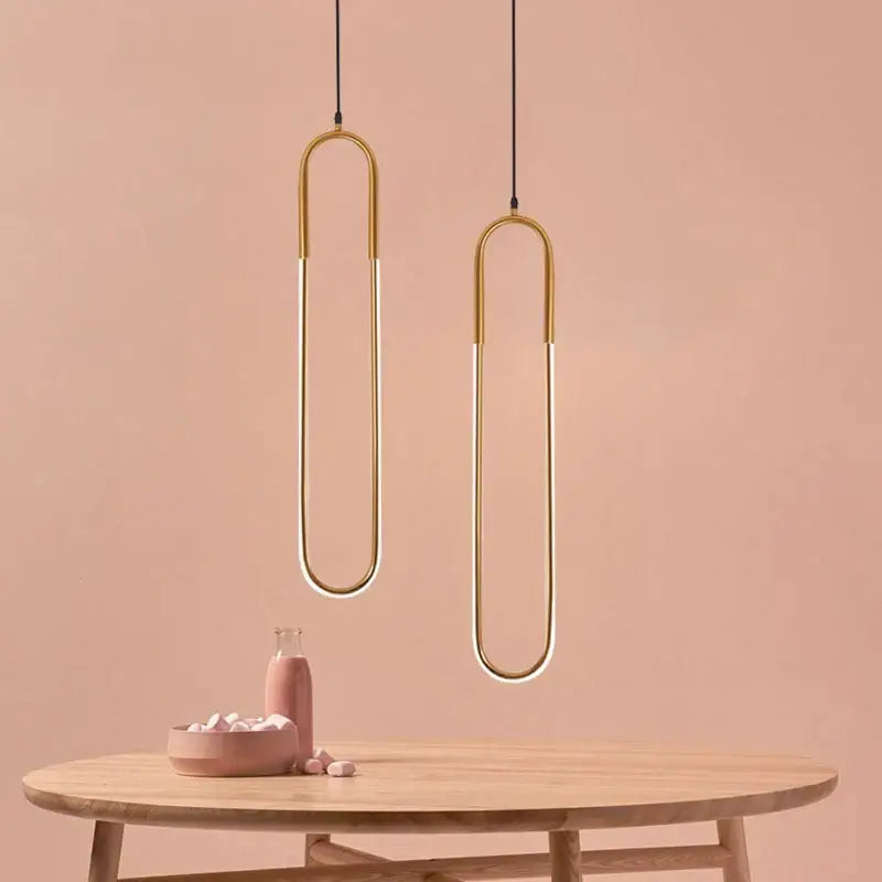 Two minimalist gold-toned led u-shaped bar chandelier pendant lights hang above a wooden table for dining room use