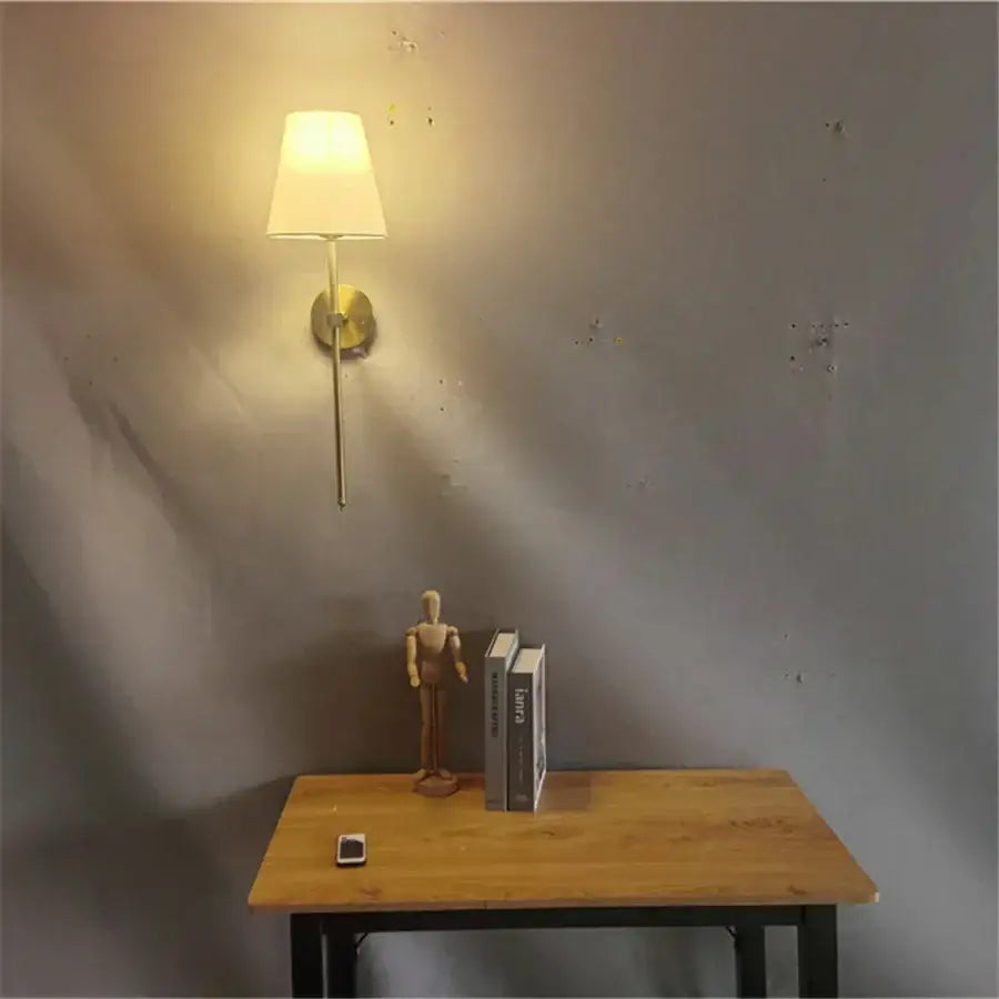 A modern brass led wall sconce with a white fabric shade and slender metal stem ideal for bedroom decorbites led wall