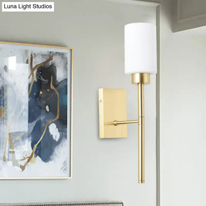 Modern brass wall light with gold-toned fixture and cylindrical white opal glass tube shade for bedroom sconce lighting