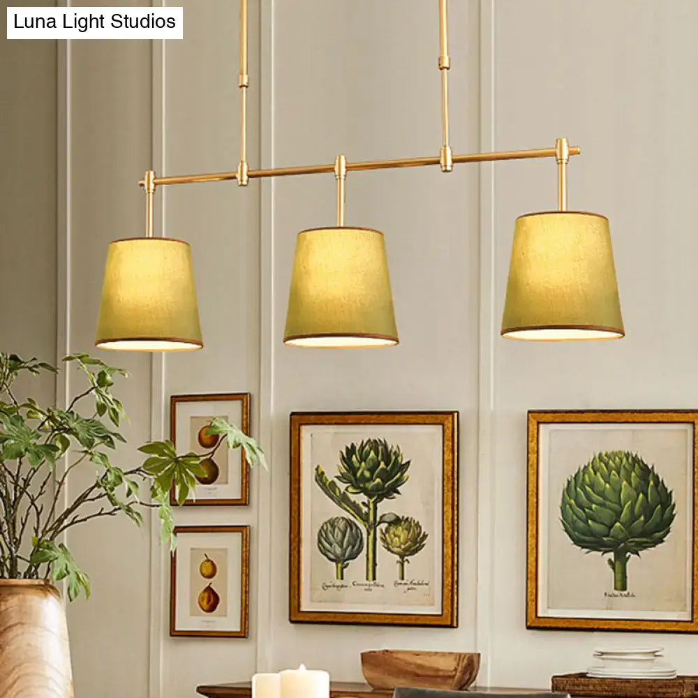 Modern brass pendant light with white green flaxen fabric shades featuring three warm-toned cylinders for dining room use