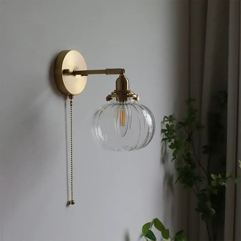 Modern brass wall sconce with decorbites glass ball, ribbed globe, edison bulb, and pull-chain switch for bedroom light