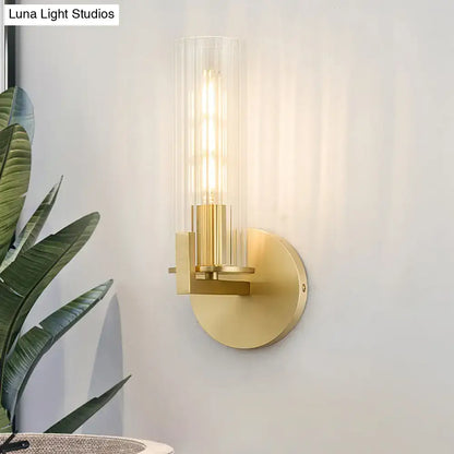 Modern brass wall sconce with gold tone finish and clear glass shade housing an exposed filament bulb for bedroom lighting