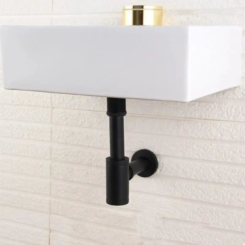 White rectangular wall-mounted sink with black matte pipe and modern brass round siphon p-trap set in gun grey
