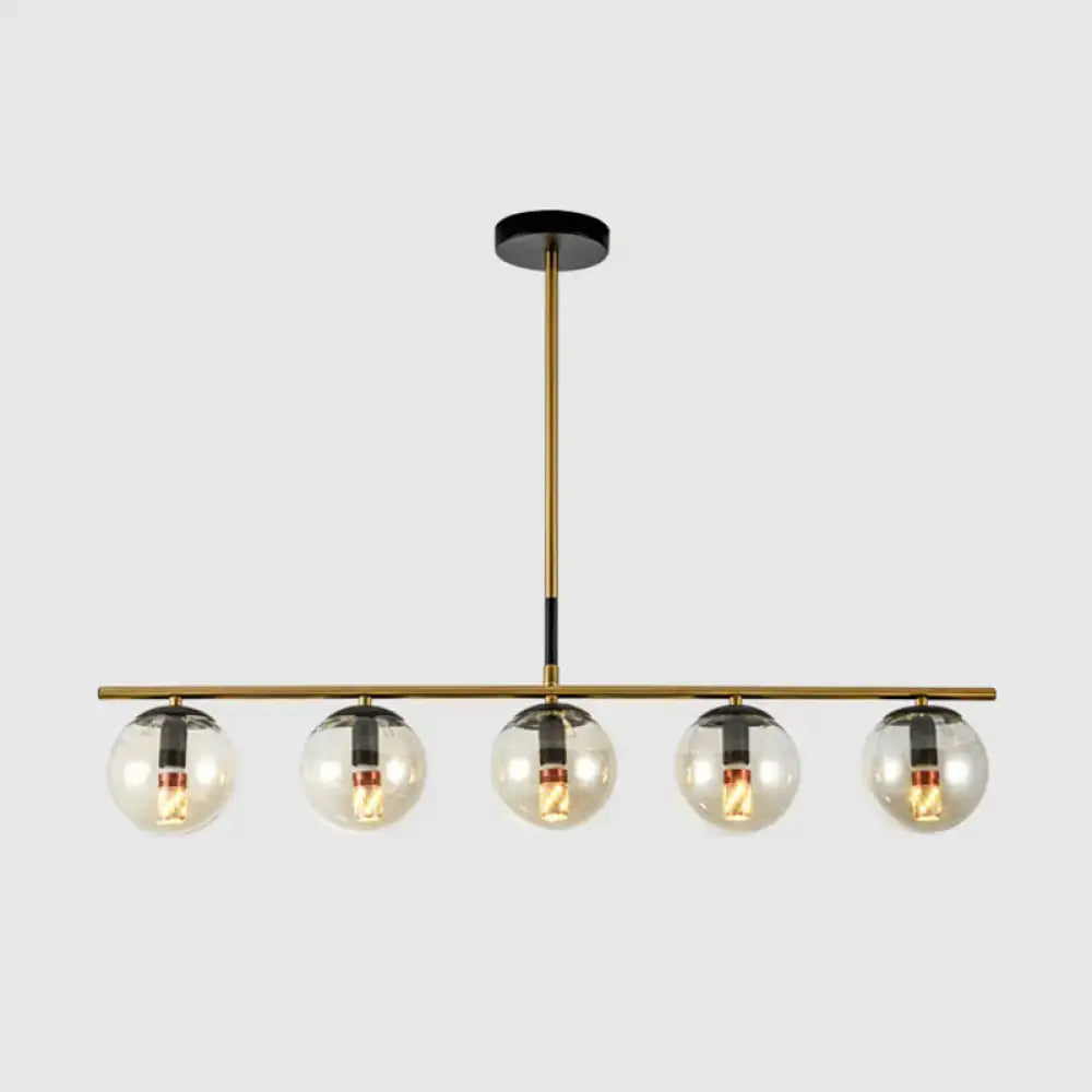 Modern brass and smoke grey globe chandelier featuring five clear glass globes with black accents for kitchen island lighting