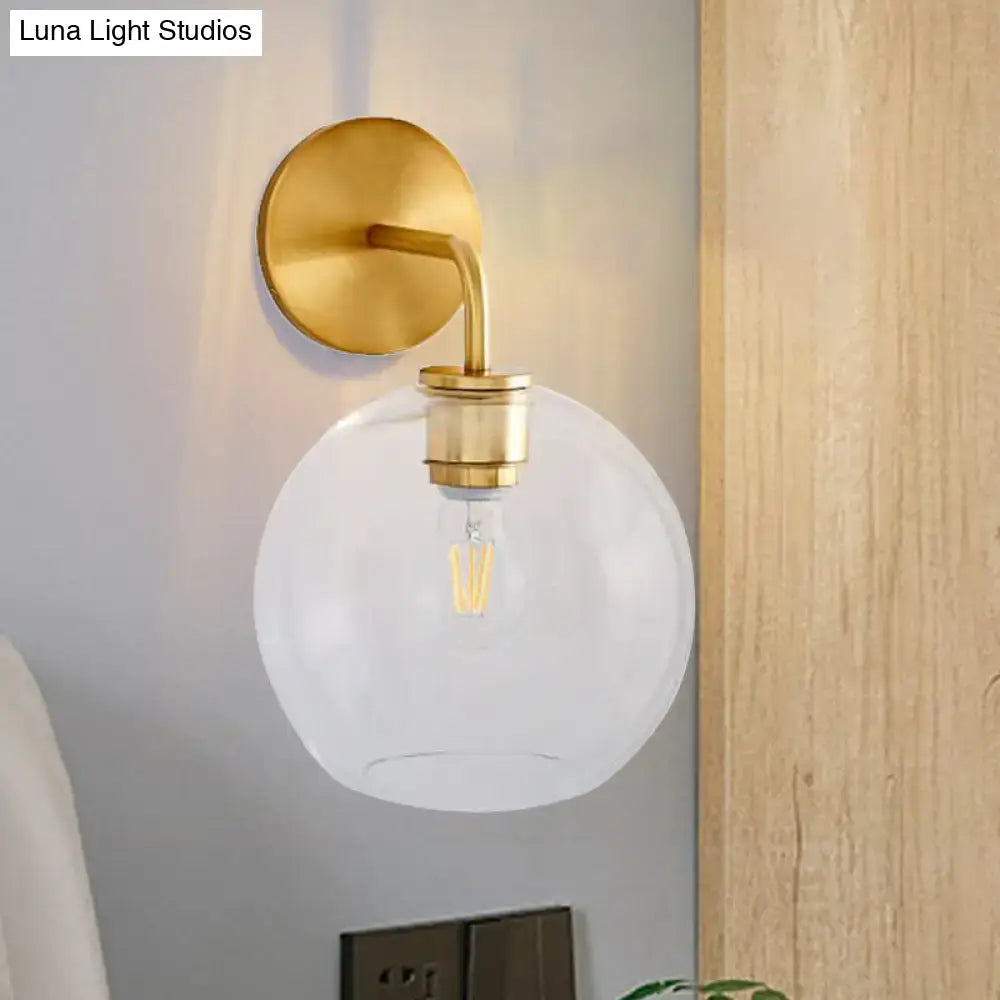 Modern brass wall lamp with gold tone sconce and clear white glass globe featuring an exposed filament bulb for bedroom use