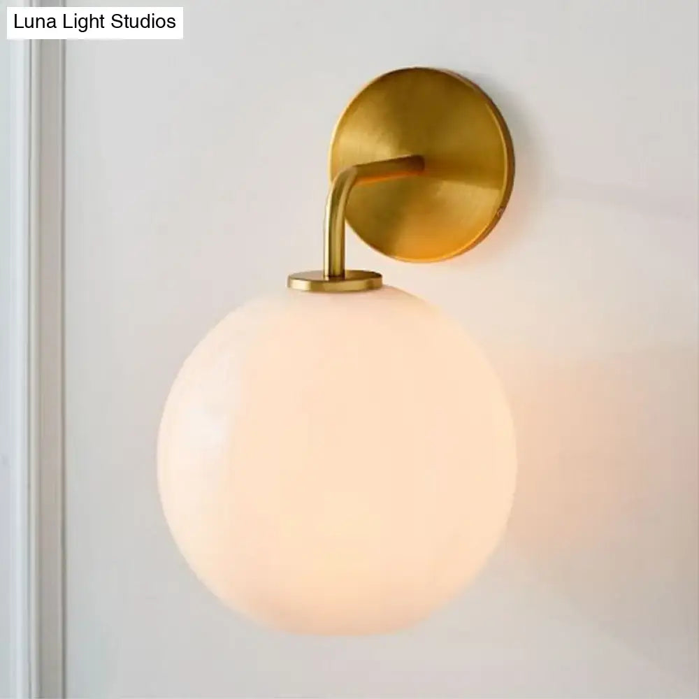 Modern brass wall lamp with gold finish and frosted clear white glass globe for bedroom lighting