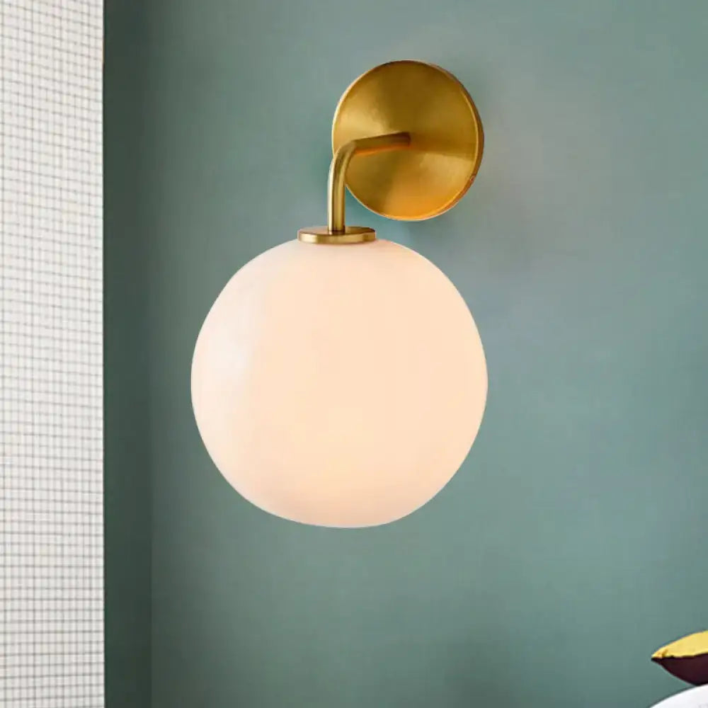 Modern brass wall lamp with gold-toned sconce and clear white glass frosted globe for bedroom lighting