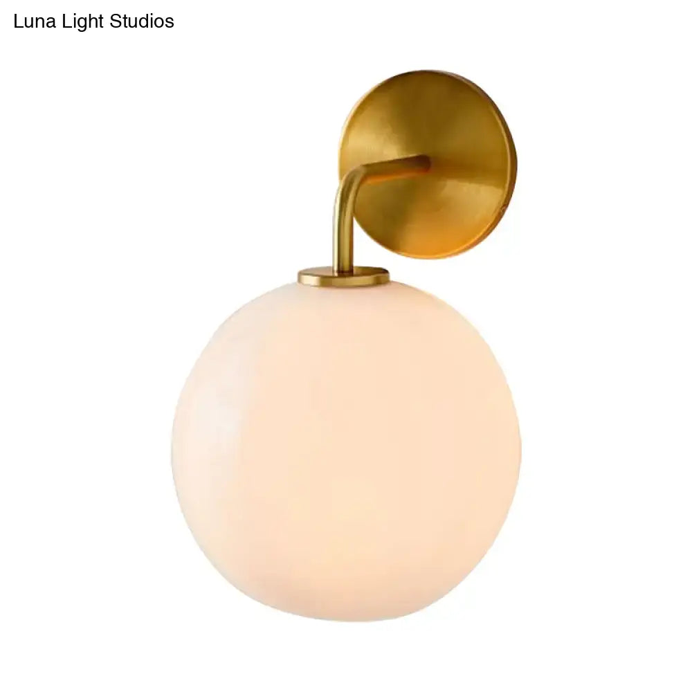 A modern brass wall lamp with a sleek finish and clear white glass globe for bedroom lighting