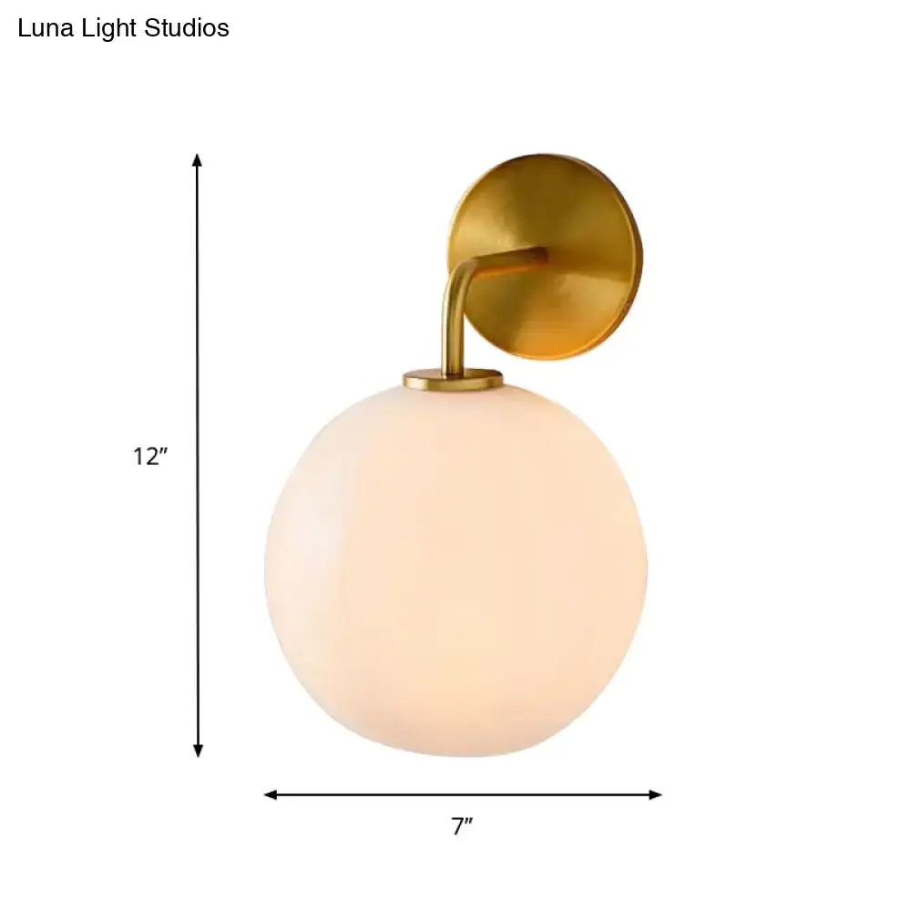 Modern brass wall lamp with a brushed brass base and clear white glass globe for bedroom lighting