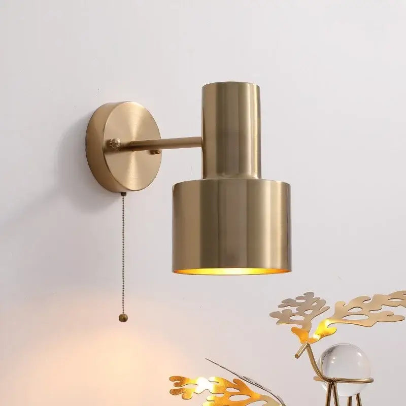 Modern brass wall lamp with brass finish and cylindrical shade featuring a pull chain switch for bedroom decor