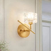 Modern brass wall light with gold-toned finish and clear crystal shade for elegant bedroom sconce lighting