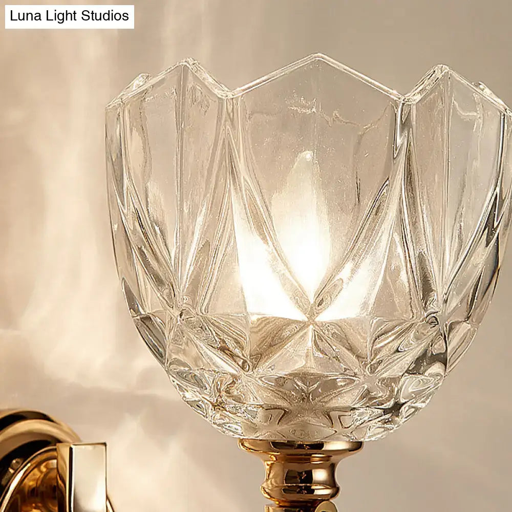 Modern brass wall sconce with a gold-toned finish and a faceted clear glass shade for bedroom lighting