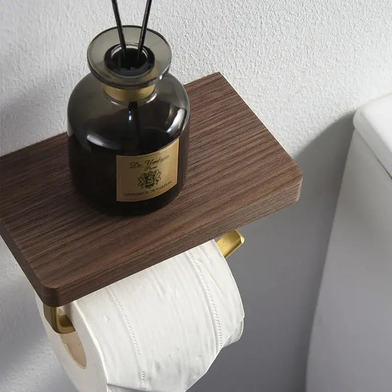 Modern brass and wood toilet paper holder with shelf features dark amber glass reed diffuser on wooden shelf above toilet paper