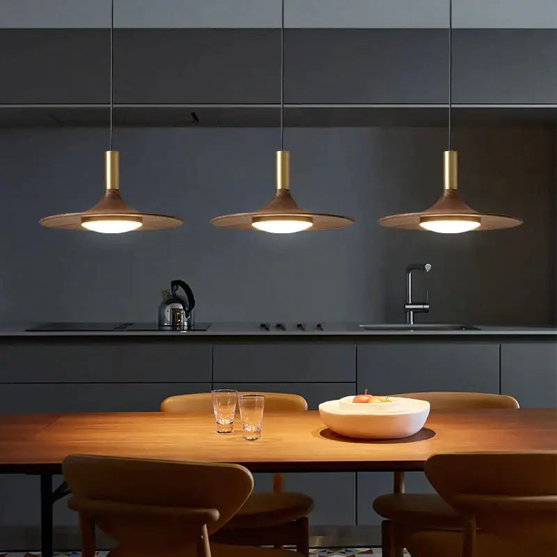 Three modern pendant lights with brass stems and decorbites black walnut ufo wooden shades above dining table