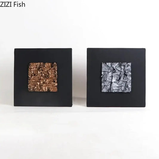 Two square modern bronze and silver gilded fabric wall art pieces with textured metallic centers and black matte frames