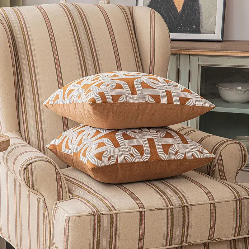 Two stacked square throw pillows with brown coffee geometric cushion cover featuring white embroidery on striped chair