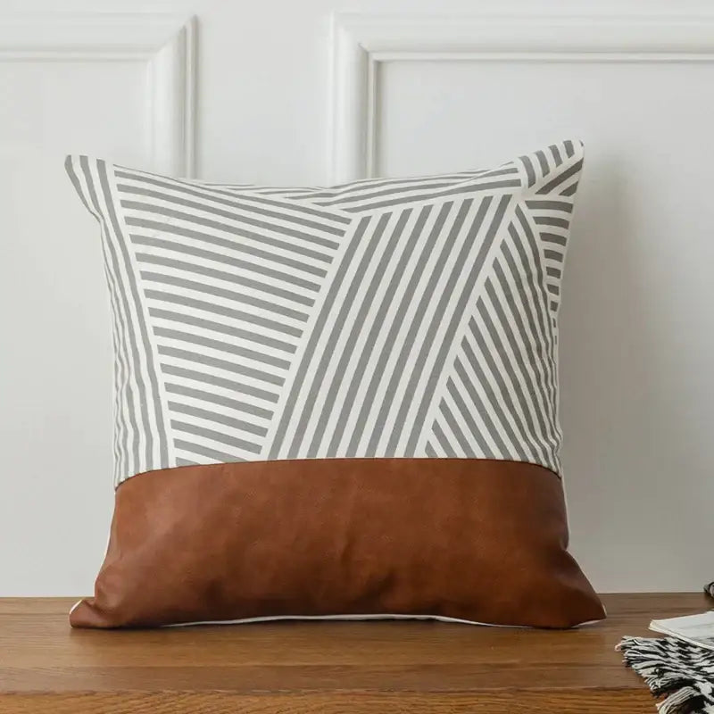 A modern square pillow cover with gray and white geometric stripes above a decorbites brown faux leather band
