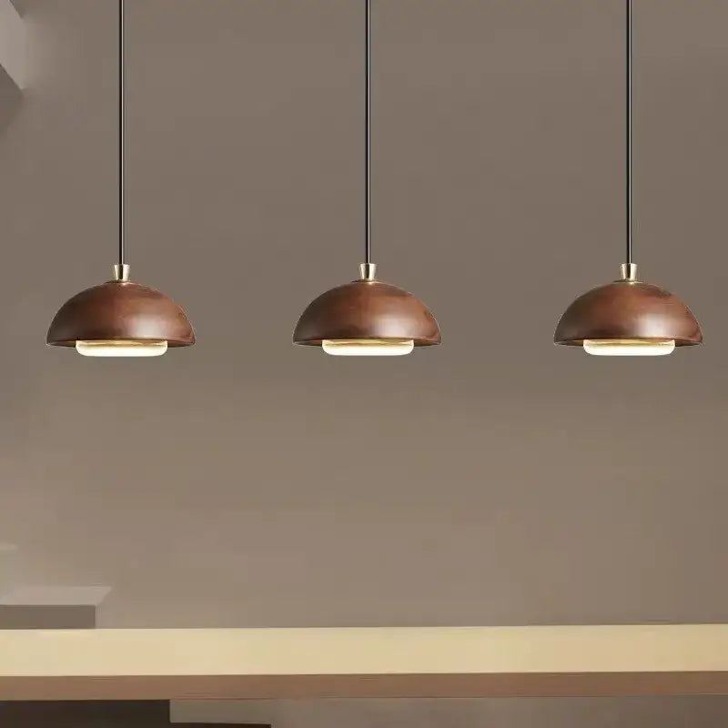 Three modern pendant lights with warm matte copper dome shades and black cords for kitchen island brown finish
