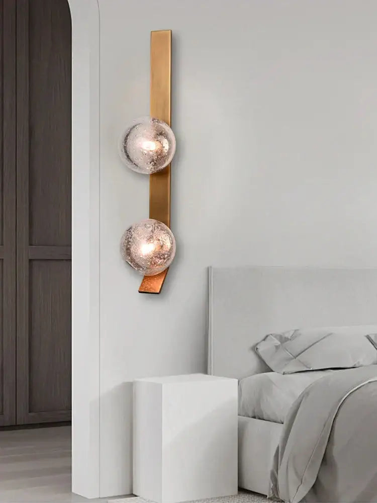 Modern brushed brass wall sconce lamps with two frosted glass spheres mounted on a vertical bar for bedroom use