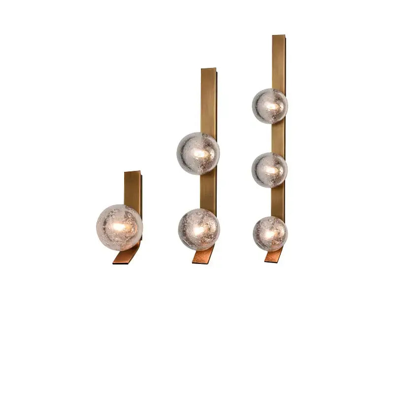 Set of three modern wall sconce lamps with brushed brass bars and frosted glass spheres for bedroom decor