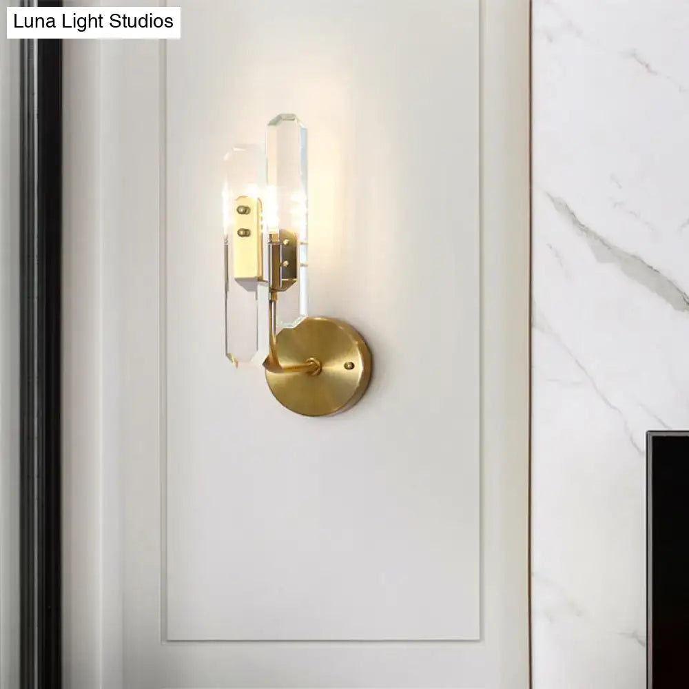 Modern brushed brass wall mounted sconce light with gold tone and clear crystal shade for living room use