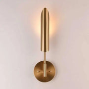 A sleek brushed brass wall lamp with a slender cylindrical shade and circular base for decorbites golden wall decor
