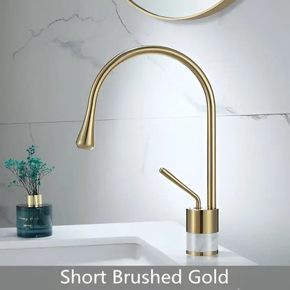 Modern brushed gold brass bathroom sink faucet with short curved spout and clear marble cylindrical base accent