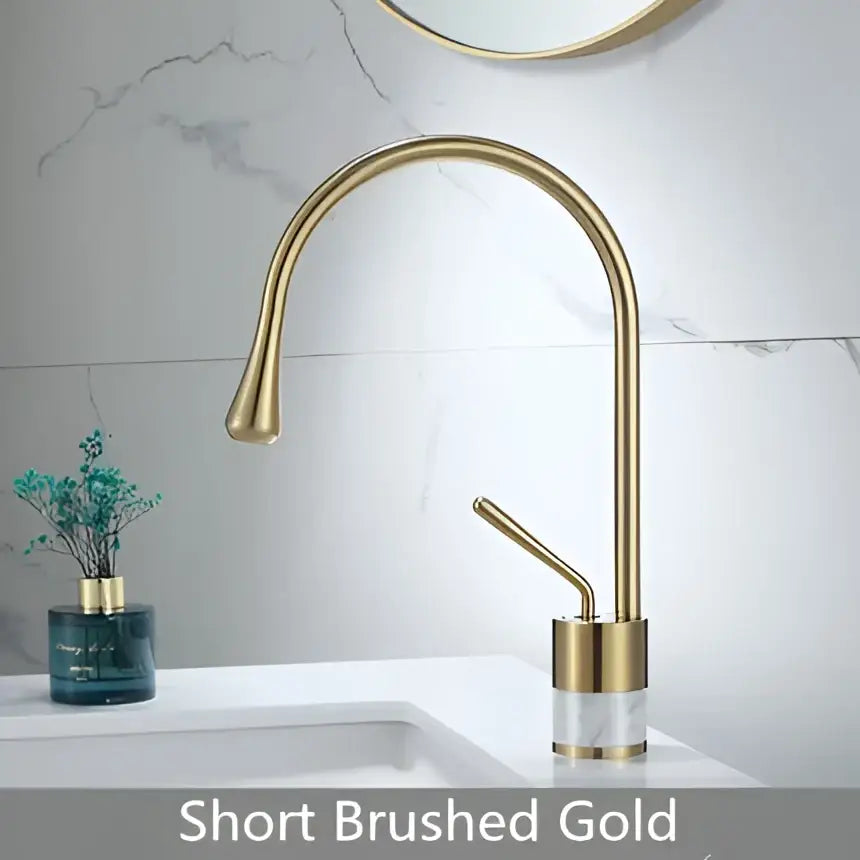Modern brushed gold brass bathroom sink faucet with short curved spout and clear marble cylindrical base accent