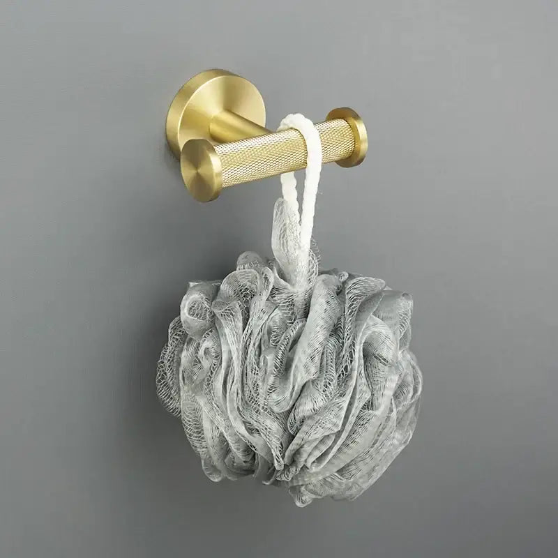 A brushed gold wall-mounted towel rack from decorbites bathroom accessories holding a gray mesh loofah with white rope