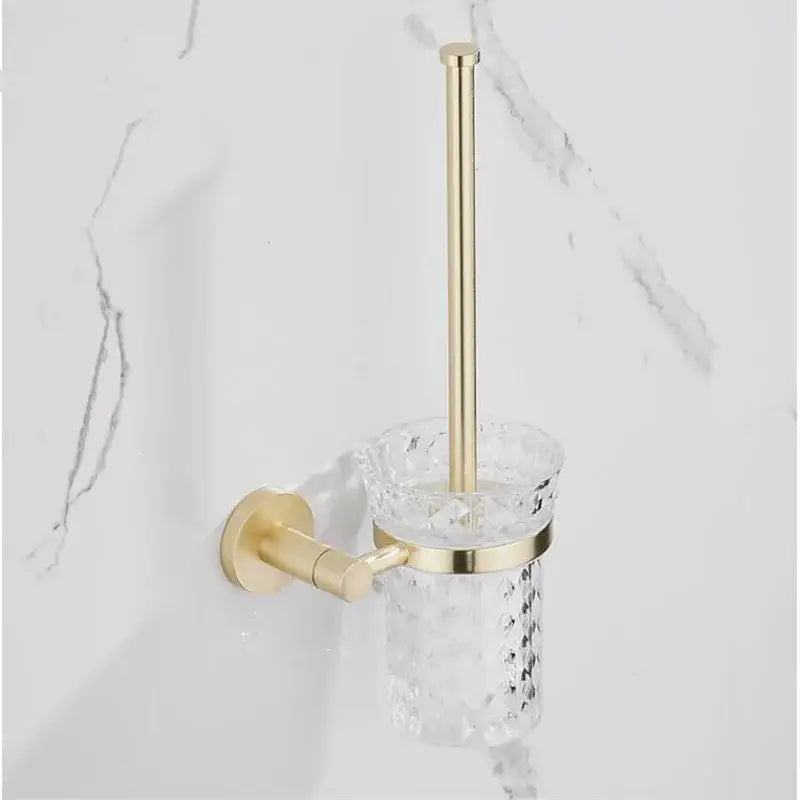 Modern brushed gold bathroom hardware set featuring a gold-toned toilet brush holder with faceted glass cup and brass mount
