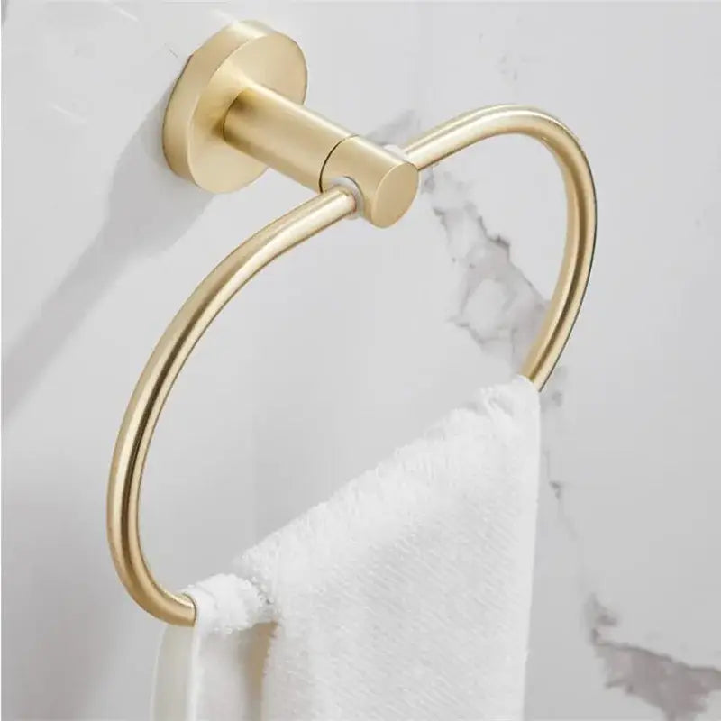 Gold-toned metal towel ring with sleek circular design mounted on wall part of modern brushed gold bathroom hardware set