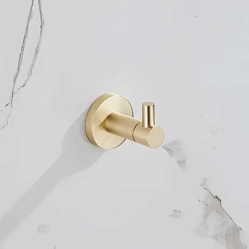 Gold-toned wall-mounted hook with circular base and cylindrical arm from modern brushed gold bathroom hardware set