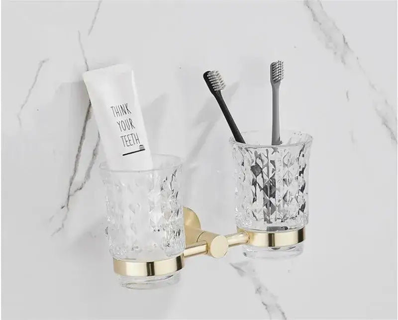 Clear faceted glass toothbrush holders with gold tone metal bases in a modern brushed gold bathroom hardware set